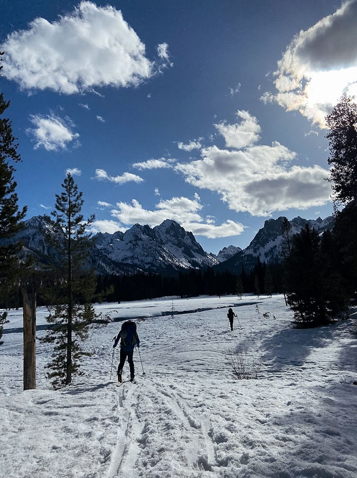 Two figures skiing across a snowy expanse towards a mountain range